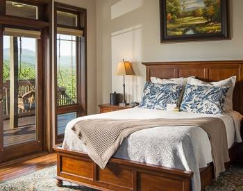 Wood platform bed with large windows looking out at the deck and Mountains 